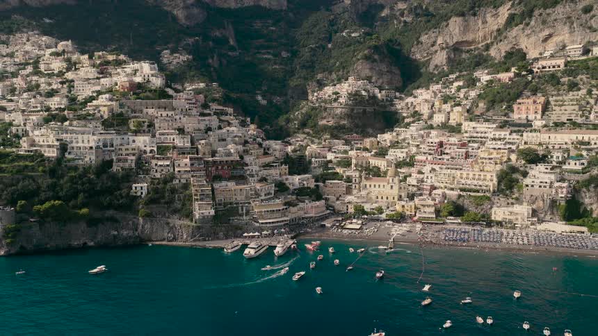 Stunning aerial shot pulling back from the picturesque cliffside town of Positano on the Amalfi Coast, Italy, revealing the bustling beach and boats on the blue sea