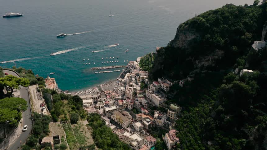 A slow aerial pullback reveals the stunning coastal town of Amalfi nestled between green cliffs on the Italian coast