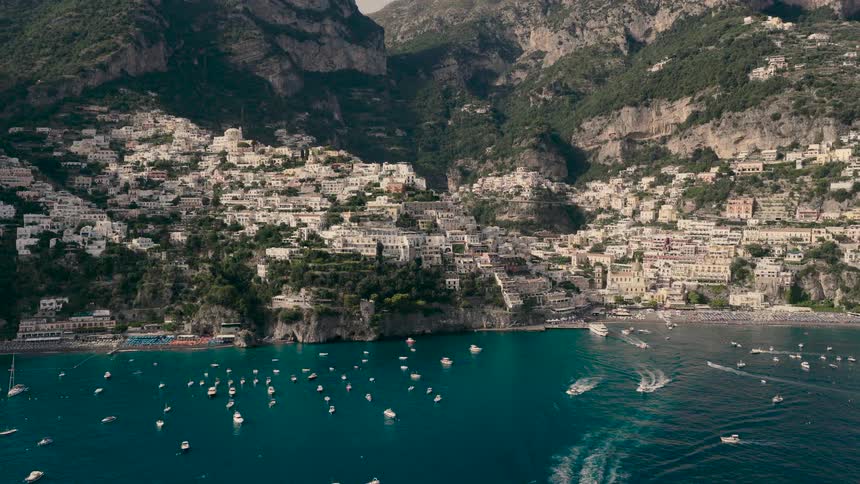 A stunning aerial pull-back reveals the picturesque cliffside village of Positano on the Amalfi Coast, with numerous boats dotting the turquoise sea