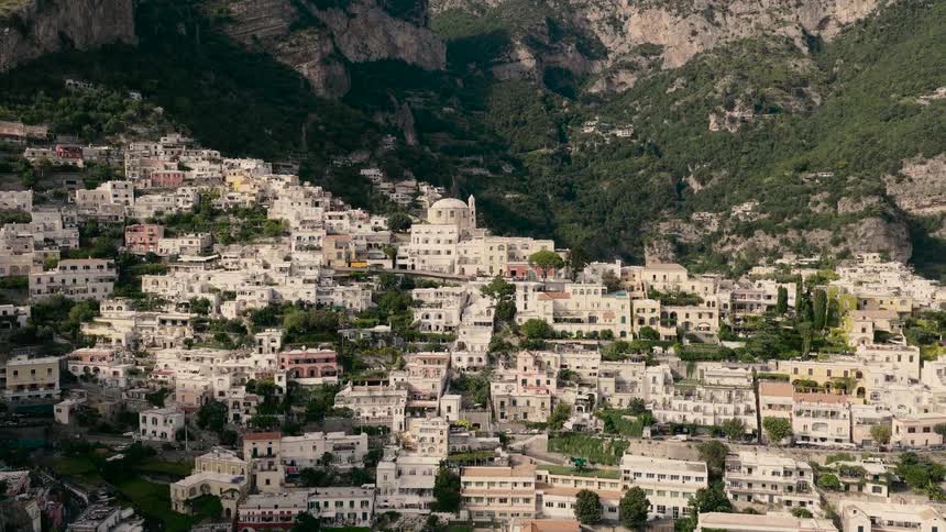 A slow aerial pullback reveals the iconic and picturesque town of Positano, nestled into the mountainside of Italy's Amalfi Coast