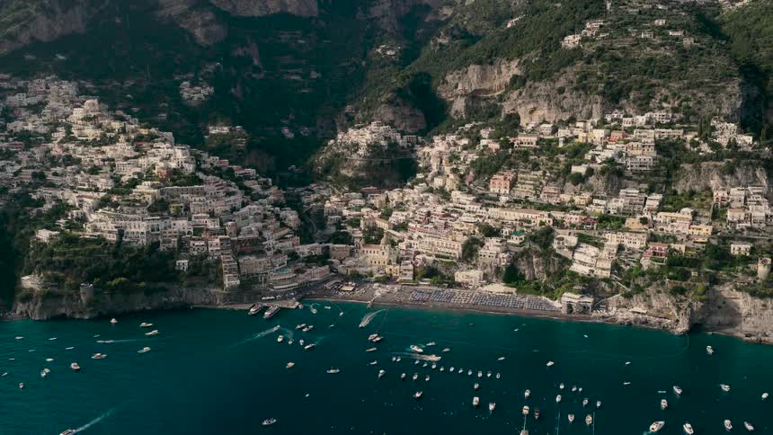 Stunning aerial view slowly pulls back to reveal the beautiful cliffside town of Positano on the Amalfi Coast, Italy, with a bustling beach and boats in the bay
