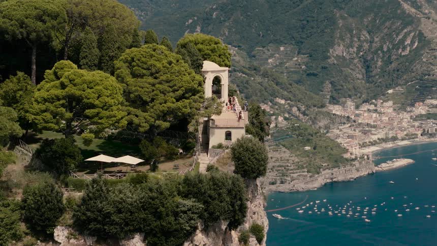 A beautiful historic villa sits on a lush green cliff overlooking the stunning Amalfi Coast in Italy