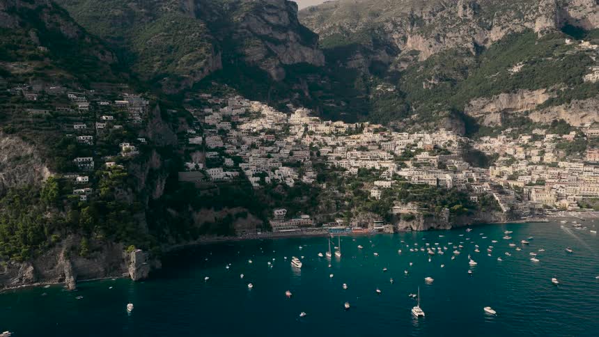 Stunning aerial view slowly approaches the iconic cliffside village of Positano on the Amalfi Coast, revealing numerous boats on the Mediterranean Sea