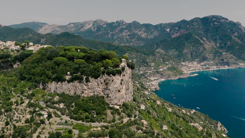 An epic aerial shot reveals the breathtaking beauty of Italy's Amalfi Coast, pushing towards a historic villa on a lush, tree-covered cliff overlooking the sea