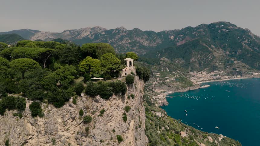 An aerial view pulls back from the lush Villa Cimbrone gardens, revealing the iconic Terrace of Infinity perched high on a cliff overlooking the beautiful Amalfi Coast