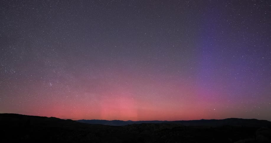 A stunning timelapse of the Aurora Australis painting the starry night sky with vibrant red, pink, and purple hues over a mountain silhouette