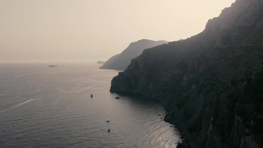 A majestic aerial view reveals the stunning and rugged Italian coastline at sunset as boats float peacefully in the sea