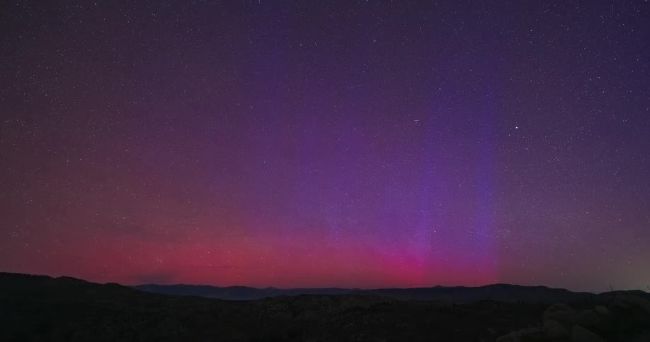 Vibrant time-lapse captures a rare red and purple aurora dancing in the starry night sky over a mountain landscape until dawn