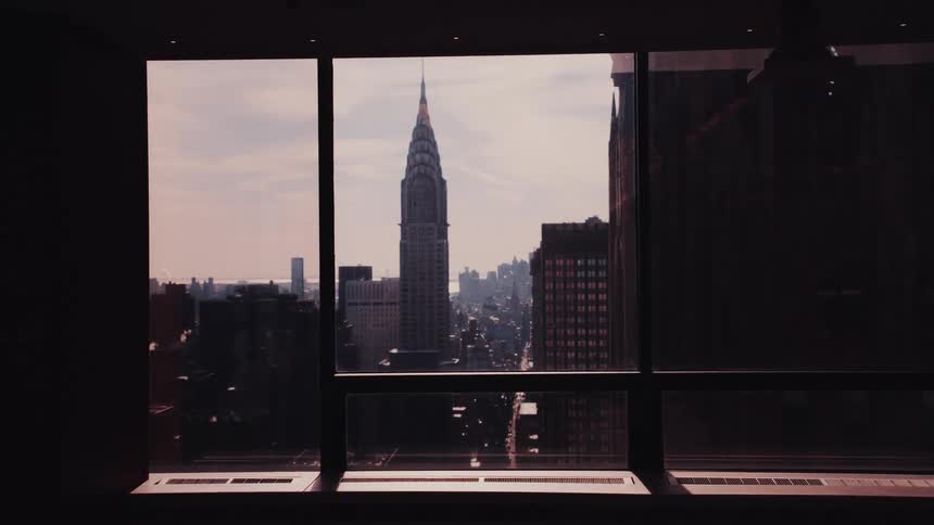 A cinematic view from a silhouetted room captures the iconic Chrysler Building in the New York City skyline