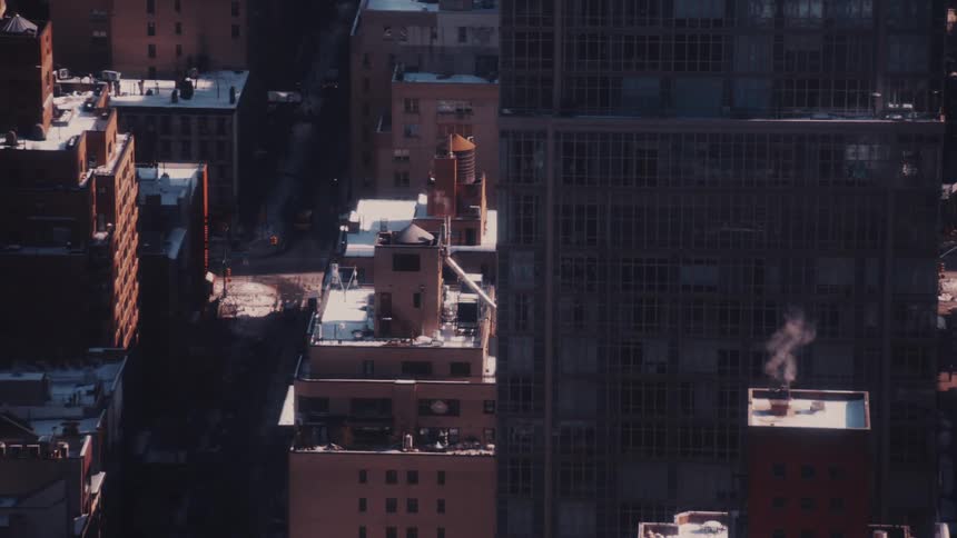 A high-angle view of snow-dusted New York City rooftops with steam rising from a chimney into the cold winter air