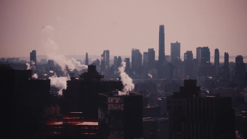 Steam rises from the rooftops of a hazy, industrial city skyline against a muted sky