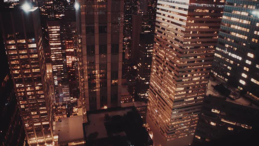 A stunning high-angle perspective of a modern city's towering skyscrapers, their windows glowing warmly in the night