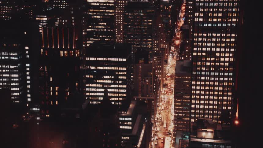 An aerial view captures the vibrant pulse of a major city at night as traffic flows through streets lined with illuminated skyscrapers