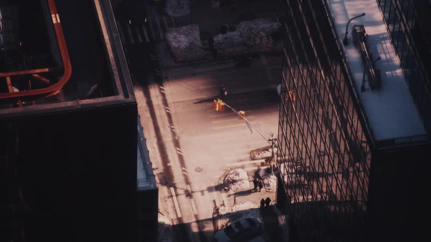 A high-angle view of pedestrians casting long shadows as they walk on a city street between skyscrapers during a winter sunset