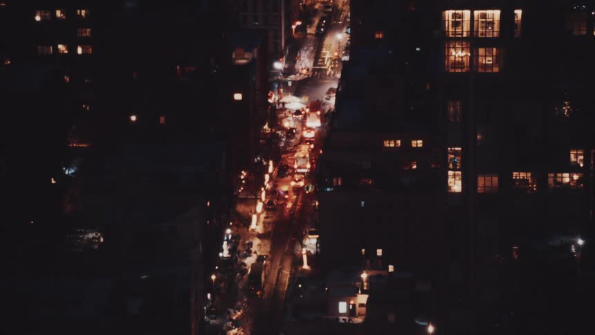 An aerial view of a busy city street at night shows heavy traffic flowing between illuminated apartment buildings