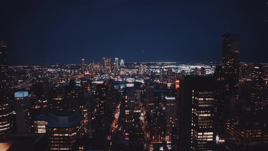 A mesmerizing wide shot captures the sprawling New York City skyline as countless lights twinkle against the deep blue night sky
