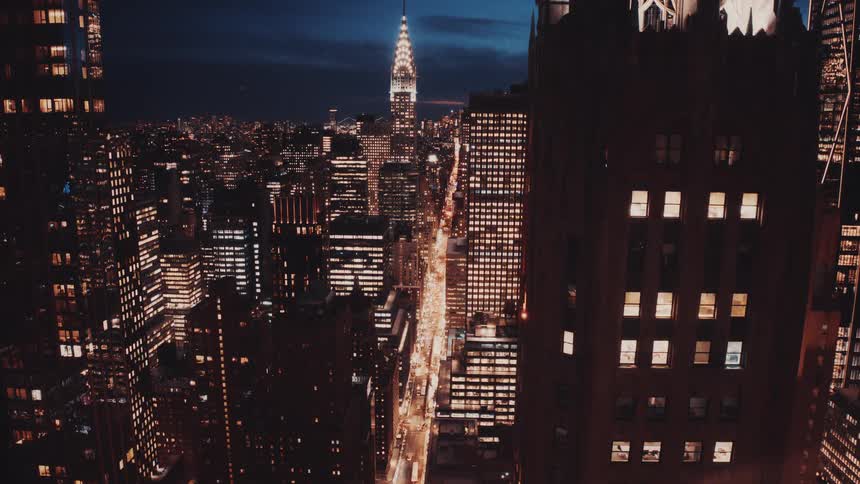 High-angle time-lapse of the iconic New York City skyline at night with the Chrysler Building and bustling city streets below