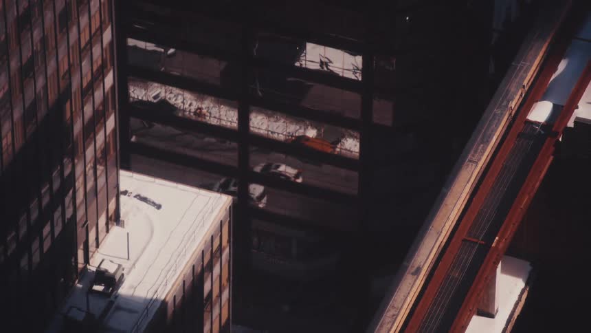 A high-angle view captures traffic and an elevated train moving through a snowy, shadow-filled city street in winter