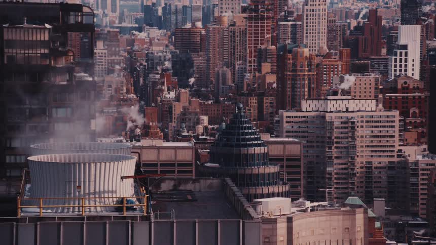 Steam rises from industrial cooling towers on a rooftop overlooking a vast and dense cityscape