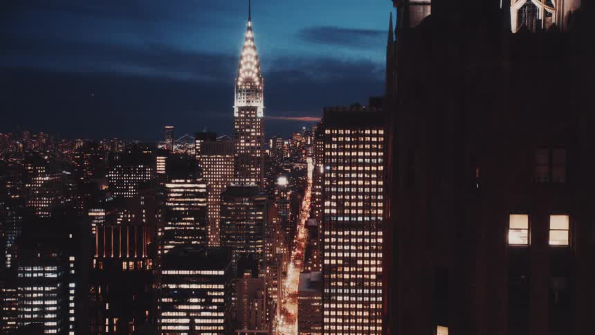 The iconic Chrysler Building stands illuminated amidst the vast, sparkling New York City skyline at dusk in a classic film-style shot