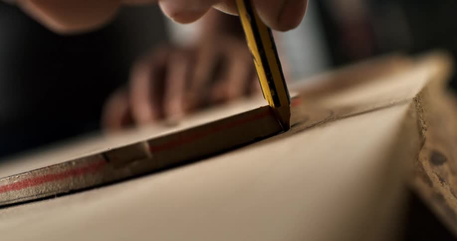 Close up of a skilled craftsman's hand carefully tracing a design onto a wooden board with a pencil