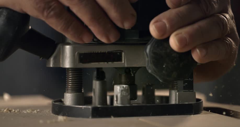 A close-up slow-motion shot of a carpenter using a router to cut into wood, with sawdust flying everywhere