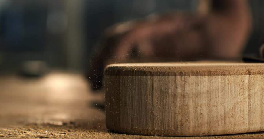 Slow-motion macro shot of a carpenter sanding the edge of a round piece of wood in a workshop