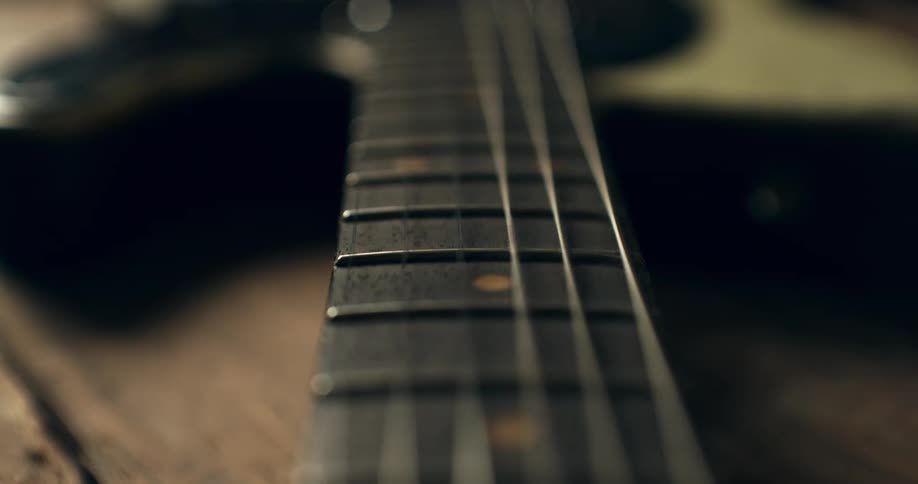 An extreme close-up dolly shot reveals the vibrating strings on the fretboard of a vintage electric bass guitar
