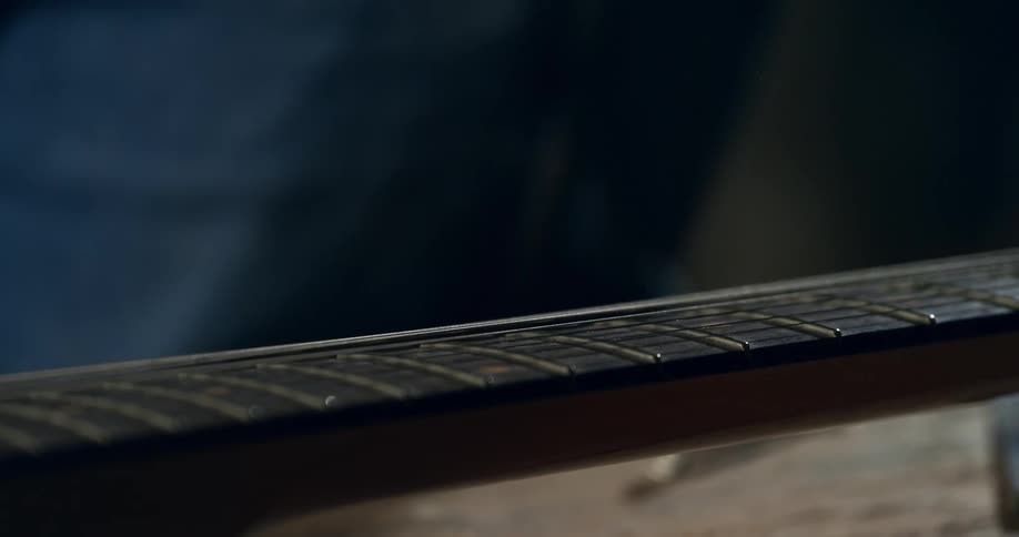 A close-up shot of a musician's hand plucking a string on a guitar fretboard, causing it to vibrate in slow motion