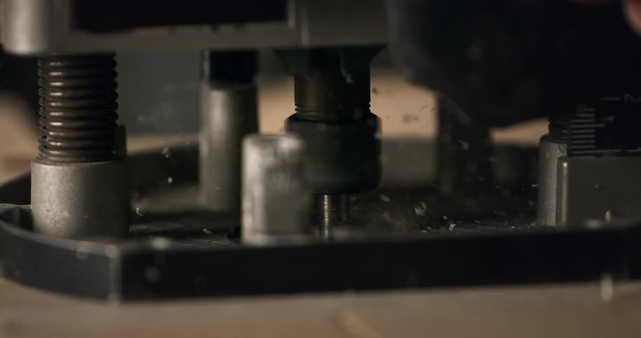 A close-up, slow-motion shot shows a wood router bit spinning and cutting into a board, sending sawdust flying