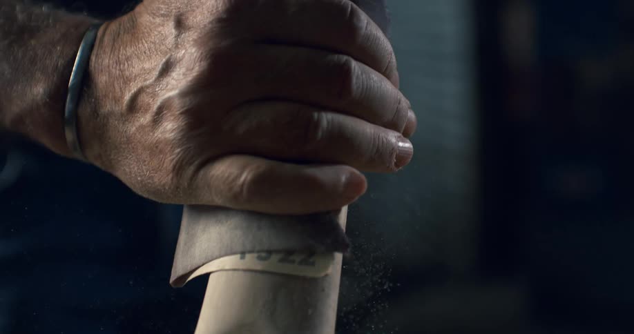 A craftsman meticulously sands a wooden furniture leg with sandpaper, creating fine dust in a workshop in slow motion