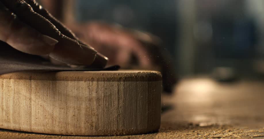 Extreme closeup of a hand sanding a circular wooden block in a dusty workshop, captured in slow motion