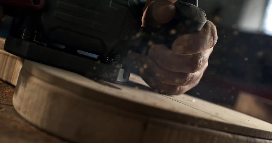 A carpenter precisely carves a piece of wood with a power router, sending sawdust flying in a dramatic slow-motion close-up