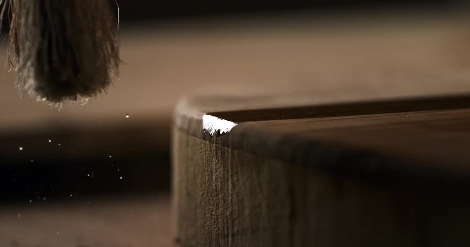 Extreme close-up of a brush applying a clear coat of varnish to a wooden surface in super slow motion
