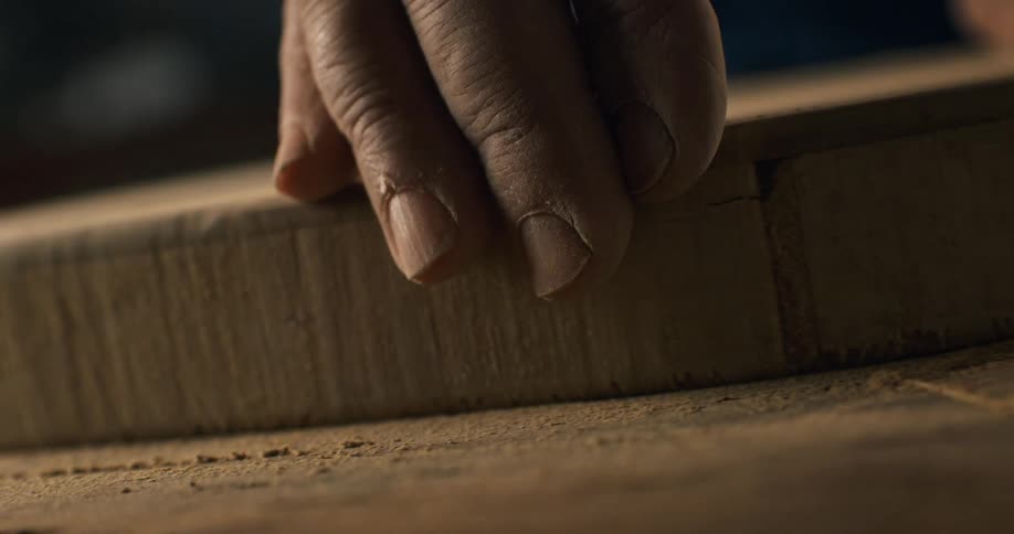 A skilled artisan's hand slowly and carefully glides along the edge of a circular piece of wood in a dusty workshop