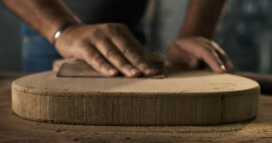 A close-up view in slow motion shows a luthier's hands carefully sanding the wooden body of a custom guitar