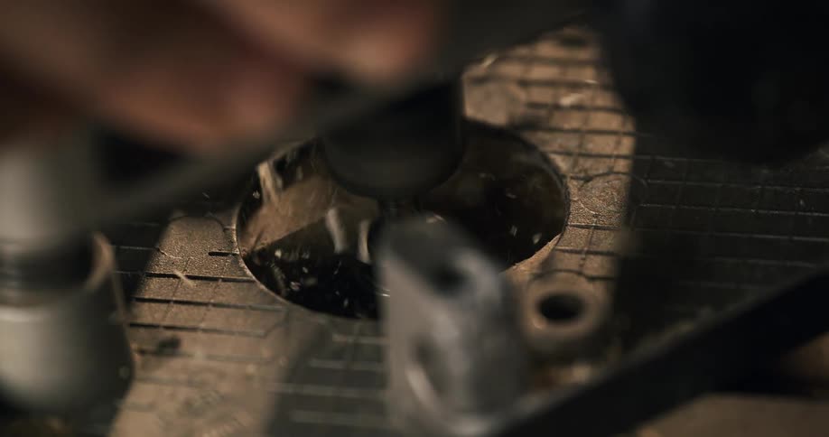 A close-up, slow-motion, top-down shot of a router bit drilling a hole into plastic, sending shavings flying