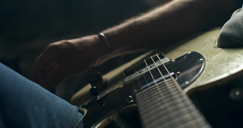 A close-up view shows a guitarist's hand strumming an old electric guitar with a pick in slow motion