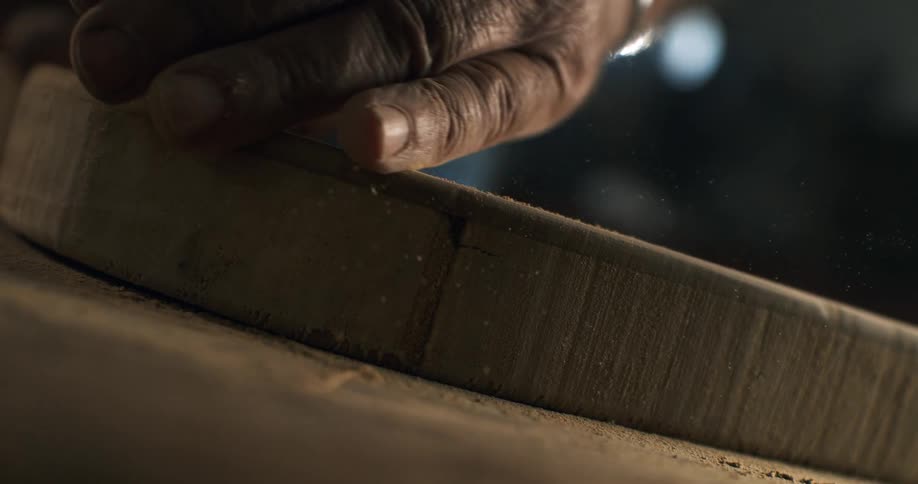 A craftsman carefully sands the edge of a wooden board in a workshop, with sawdust flying in slow motion