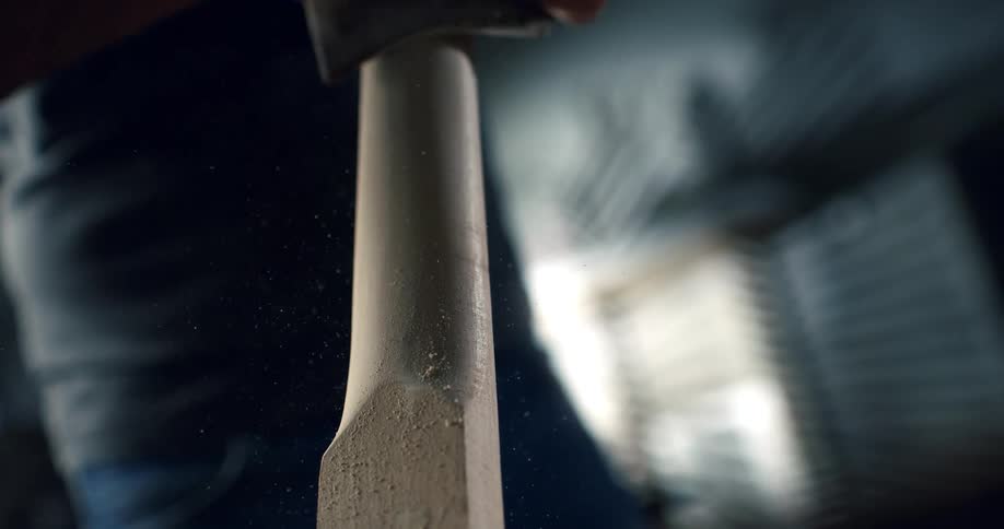 A craftsman's hands meticulously sand a wooden handle in a workshop, captured in dramatic slow motion with flying sawdust