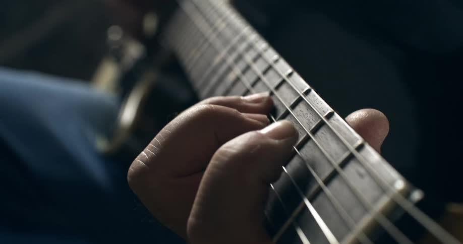 A dramatic close-up of a guitarist's fingers expertly moving along the fretboard of an acoustic guitar