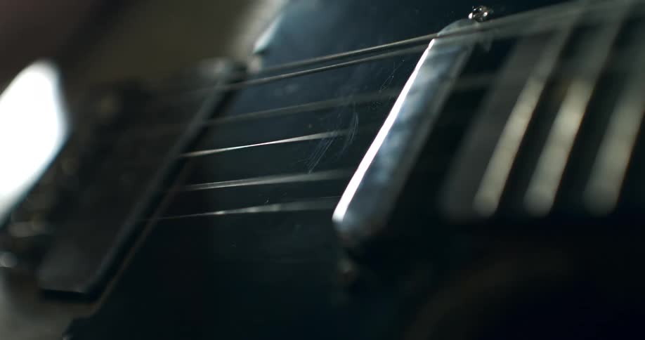 Extreme close-up of a musician strumming the strings of a dark electric guitar, showing the strings vibrating in slow motion