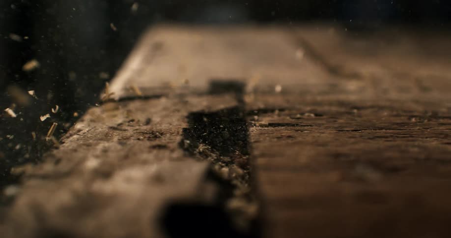 Dramatic slow motion close-up of sawdust and wood shavings being blown off a rustic wooden workbench