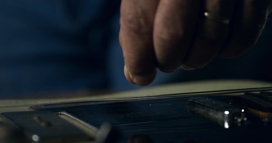 A musician's finger plucks a string on an electric guitar in dramatic slow motion