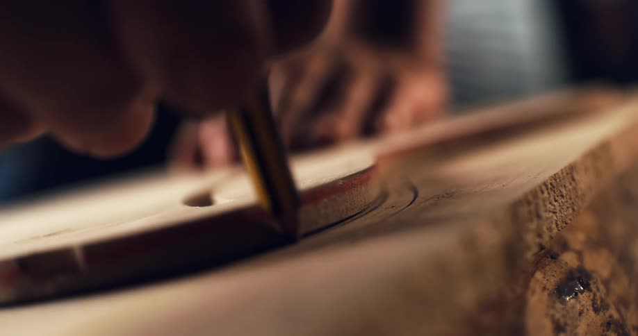 A craftsman's skilled hand carefully traces a precise circle onto a wooden board with a pencil in slow motion
