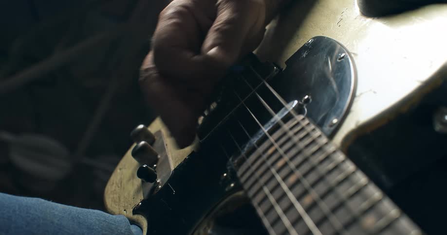 Slow motion close-up of a musician's hand strumming an old electric guitar in a dimly lit room