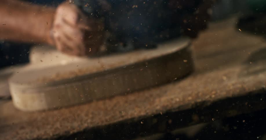 A woodworker uses a power router to shape a piece of wood, sending sawdust flying in a dramatic super slow motion shot