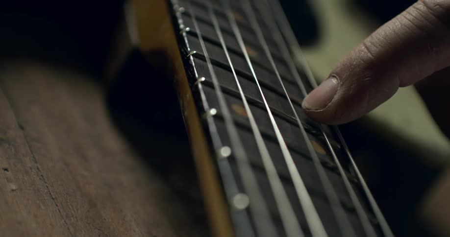 An extreme close-up shot of a musician's finger applying vibrato to a guitar string in slow motion