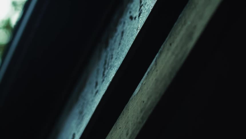 A single, mesmerizing drop of water falls in slow motion between dark, weathered wooden beams