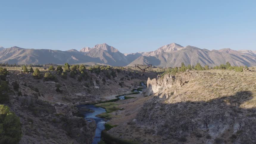 A filmmaking drone hovers and flies backwards over a beautiful river gorge with the Sierra Nevada mountains in the background